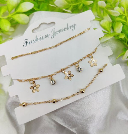 Gold bracelet set on a white card with greenery in the background