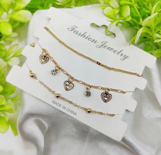 Gold heart-shaped charm necklaces on a white card with green leaves in the background