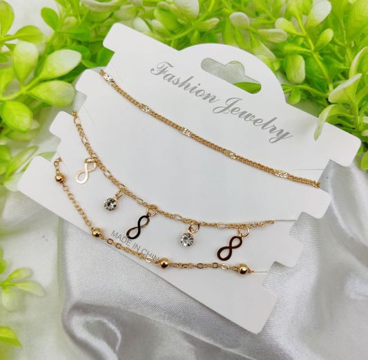 Set of layered gold necklaces on a white card with greenery in the background