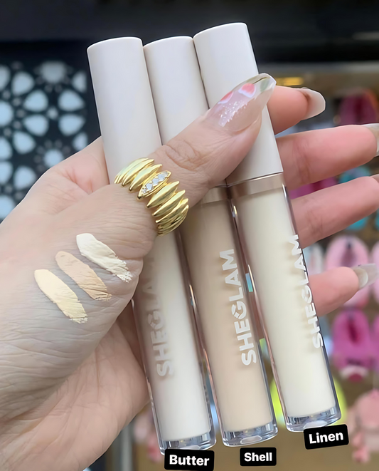 Hand holding three lip gloss tubes labeled 'Butter', 'Shell', and 'Linen' with 'SHEGLAM' branding.