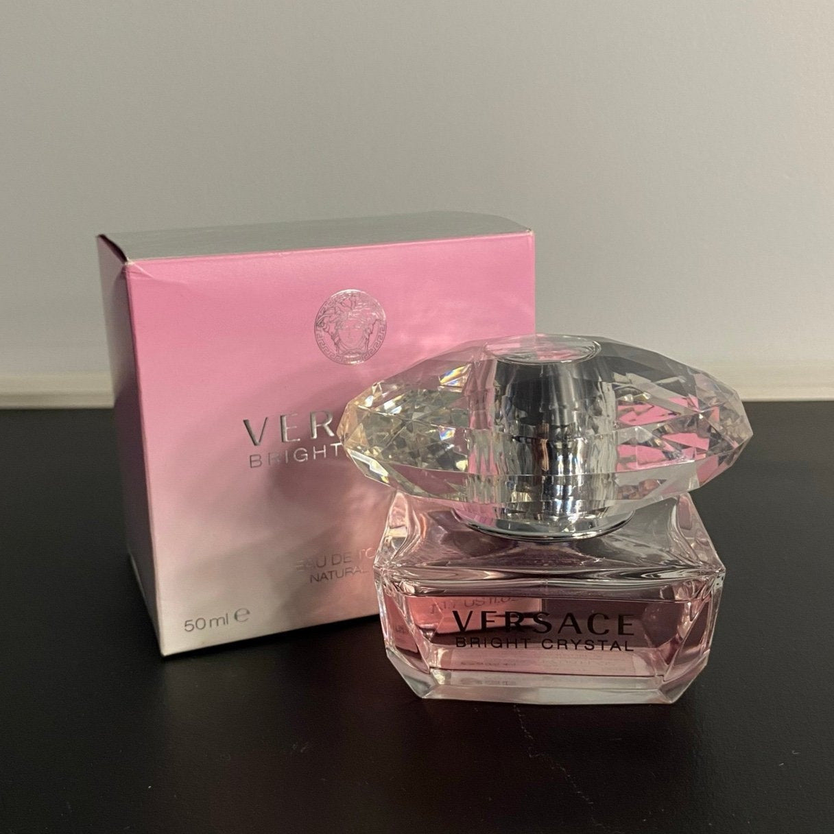 Versace perfume bottle and packaging on a black surface with a gray background