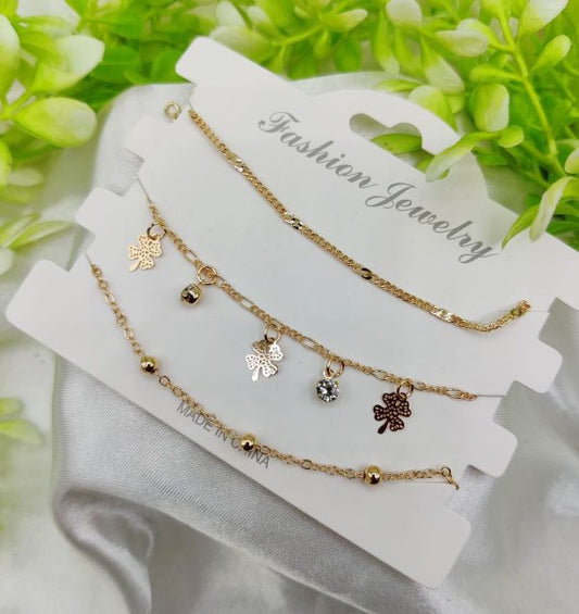 Set of gold necklaces with charms on a white card with 'Fashion Jewelry' text, against a green leafy background.